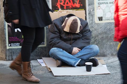 en man som sitter med nedböjt huvud och tigger pengar i en pappmugg